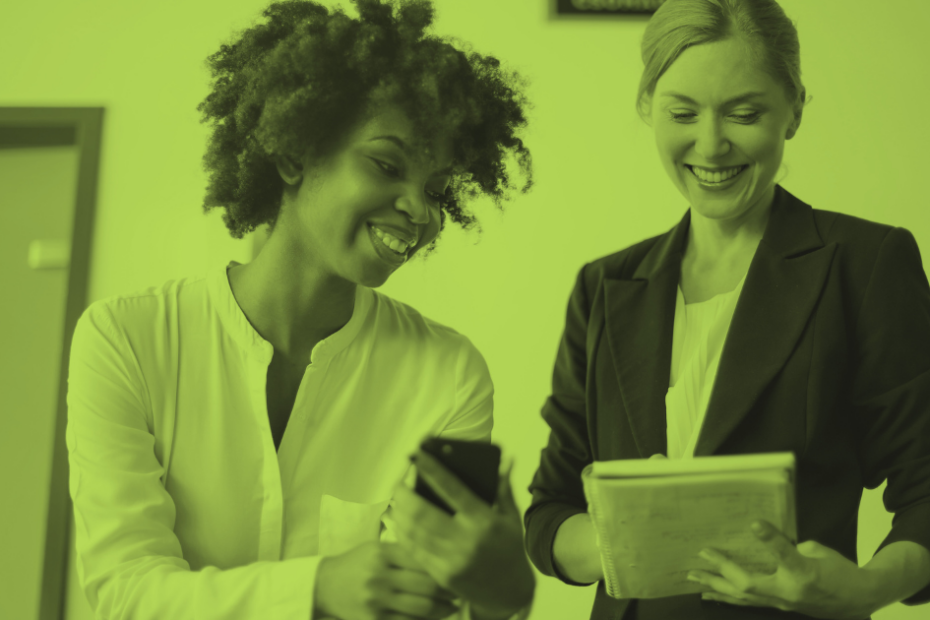 Two female coworkers smiling into their gadgets