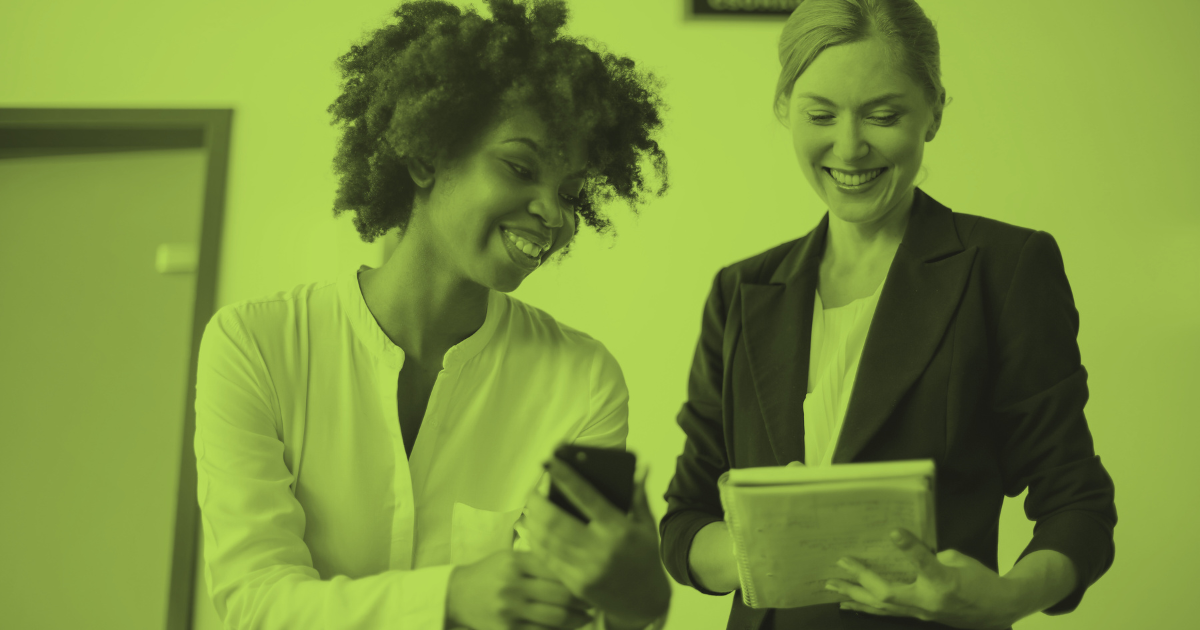 Two female coworkers smiling into their gadgets